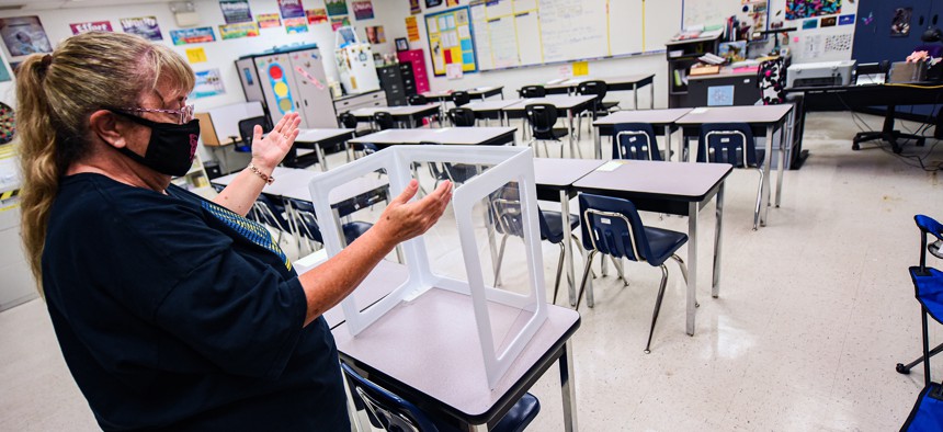 In this file photo, teacher Darlene Huntley shows how student desks were fitted with barriers last year at Lyman High School in Longwood. 